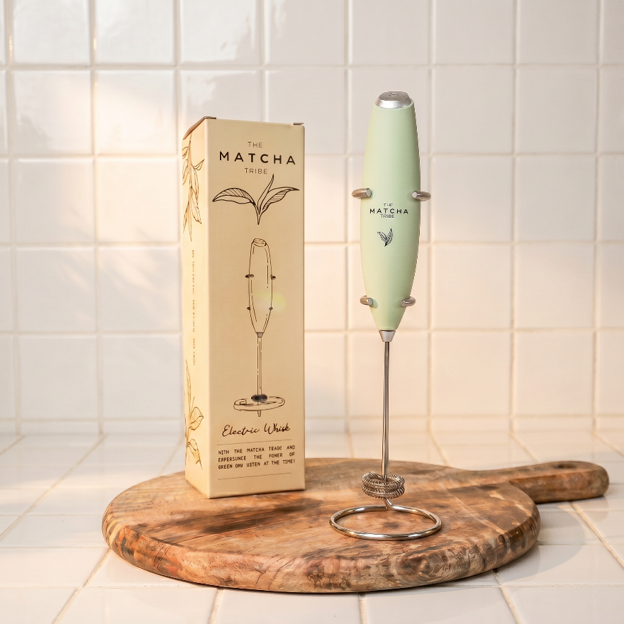 Green electric whisk with packaging on a wooden board against a tiled wall.