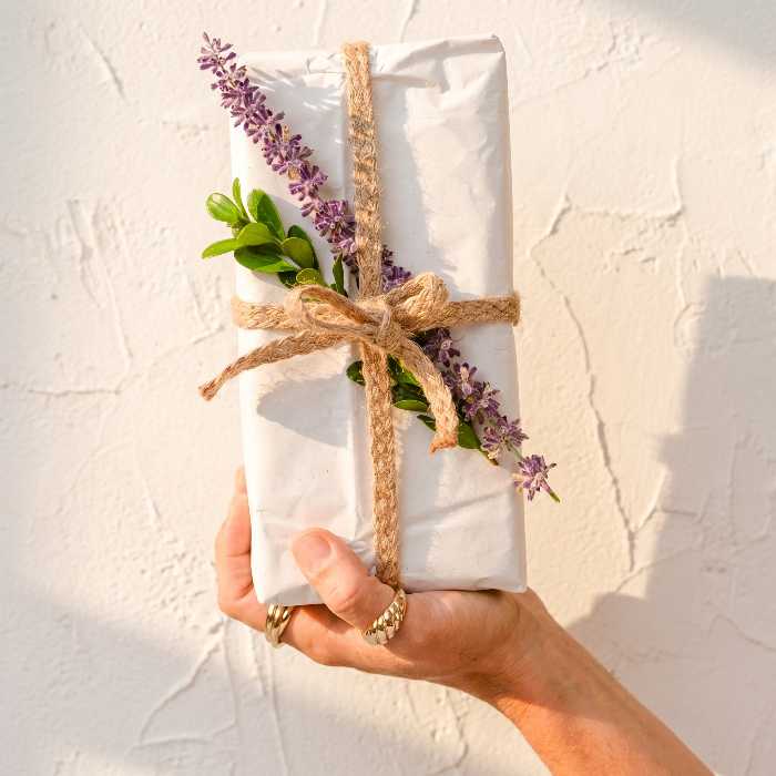 Hand holding a wrapped gift with lavender and twine against a light background